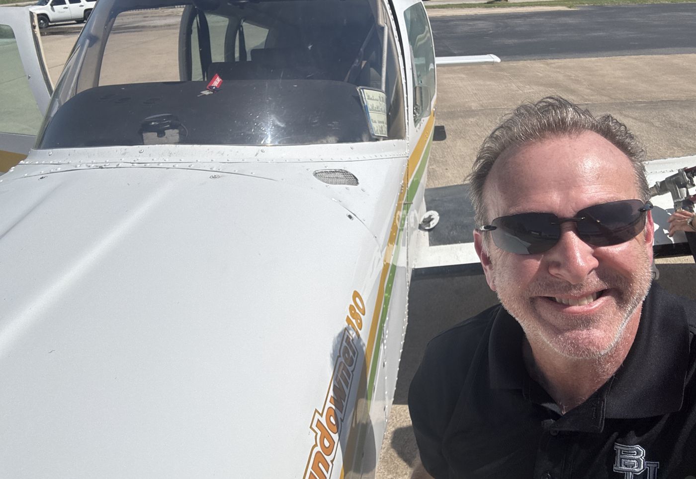Pilot smiling in front of a Piper Cherokee 180 on the ramp